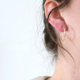 Close-up of an ear wearing a gold hoop earring on a light background