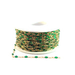 Spool of gold chain with green beads on a white background