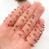 Gold chain with pink beads held in a hand on a white background