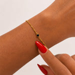 Gold bracelet with a black gemstone on a wrist with red nail polish against a light background