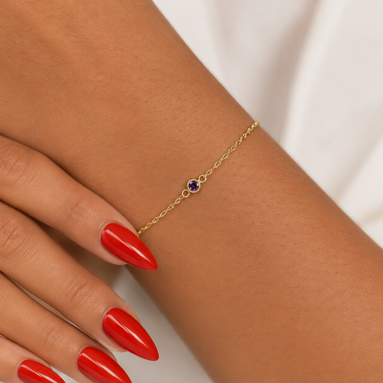 Gold bracelet with a February amethyst gemstone on a wrist with red nail polish.
