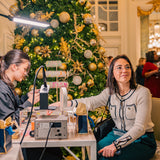 Woman getting permanent jewelry bracelet at the Willard DC corporate event for. Behind her is a festive indoor setting with a decorated Christmas tree.
