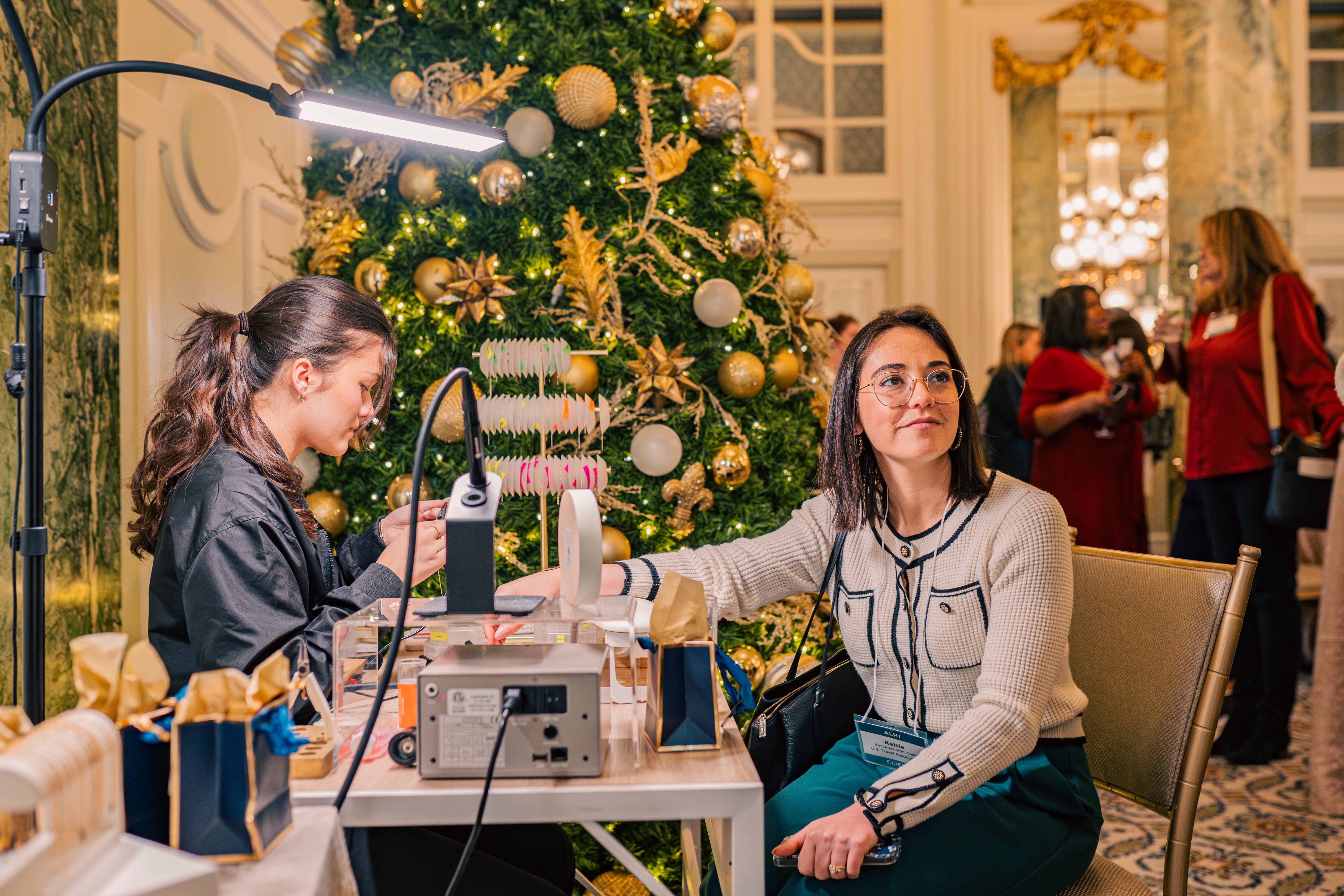 Woman getting permanent jewelry bracelet at the Willard DC corporate event for. Behind her is a festive indoor setting with a decorated Christmas tree.