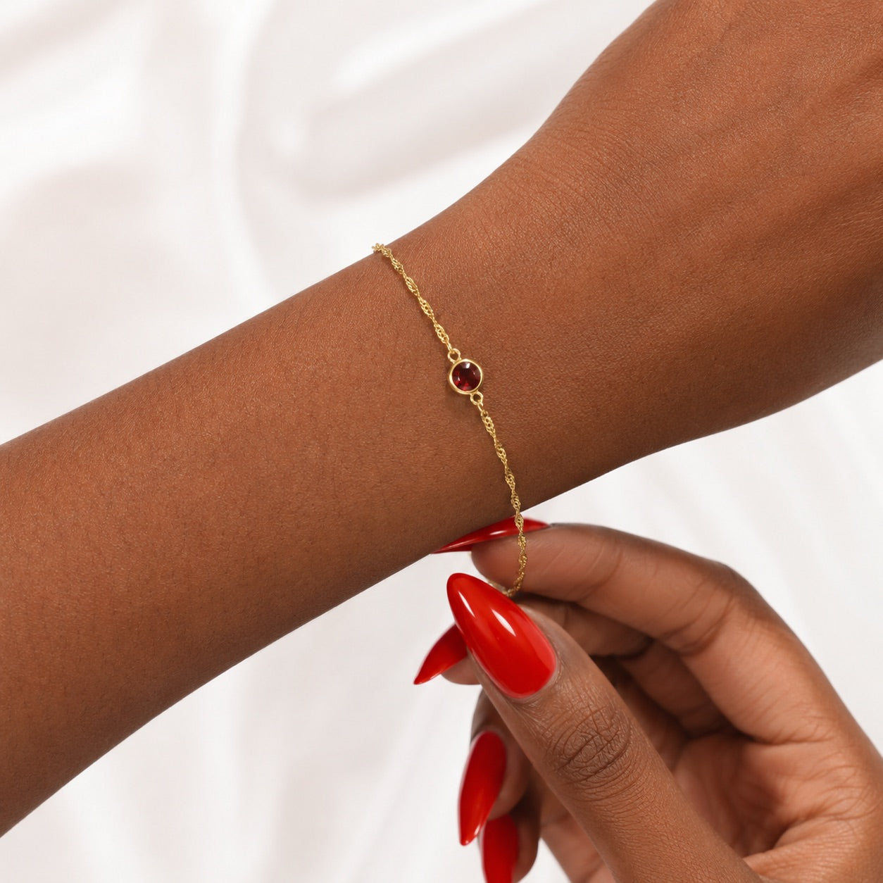 Gold bracelet with a January red garnet gemstone on a wrist against a white background