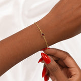 Gold bracelet with a January red garnet gemstone on a wrist against a white background