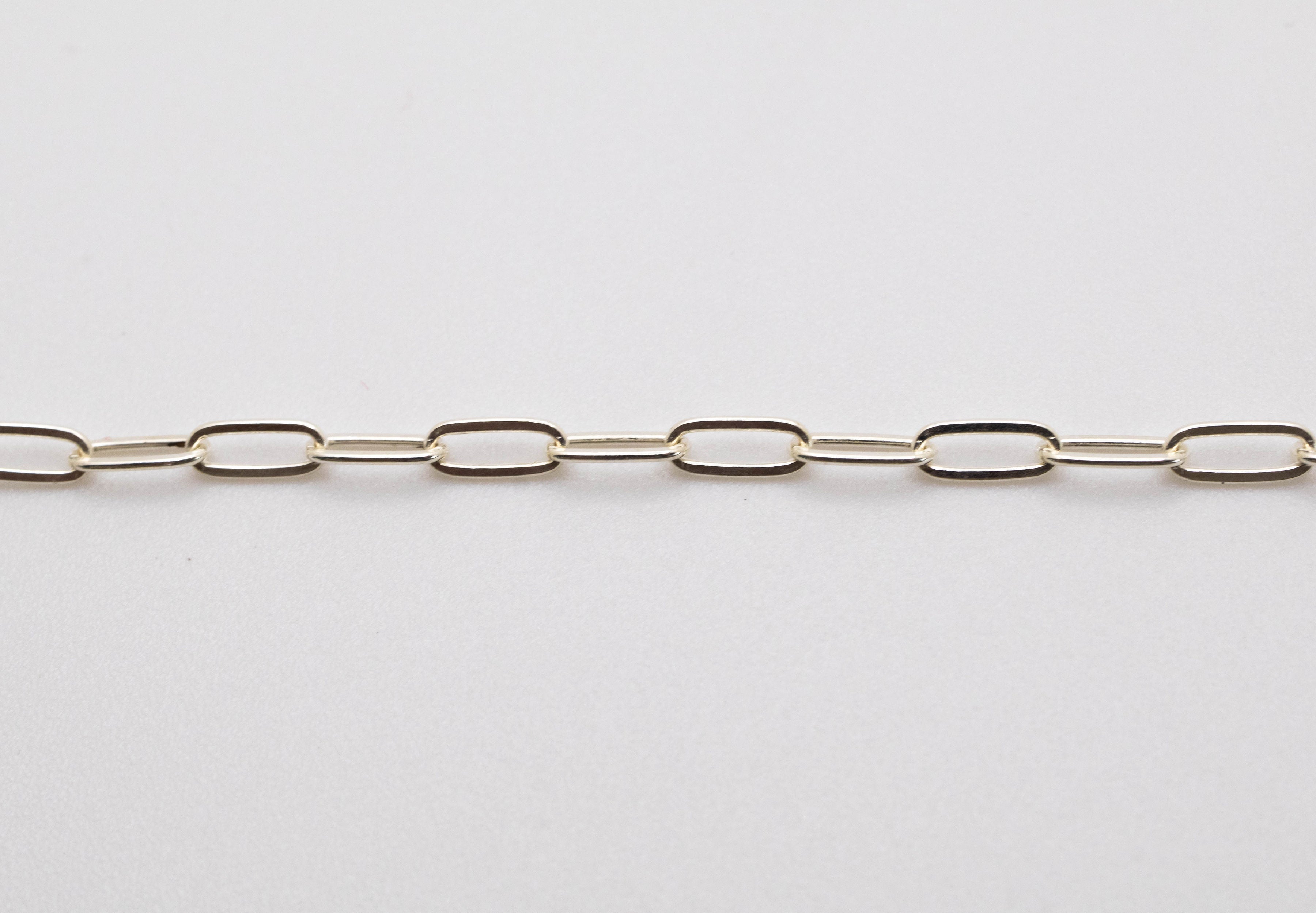 A silver paperclip chain laid out on a white surface.