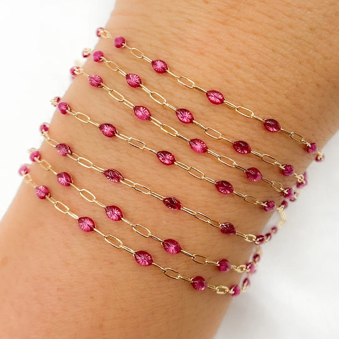 Gold chain bracelet with pink beads on a wrist against a white background