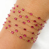 Gold chain bracelet with pink beads on a wrist against a white background