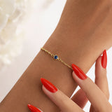 Gold charm bracelet with a September blue gemstone on a wrist with red nail polish.