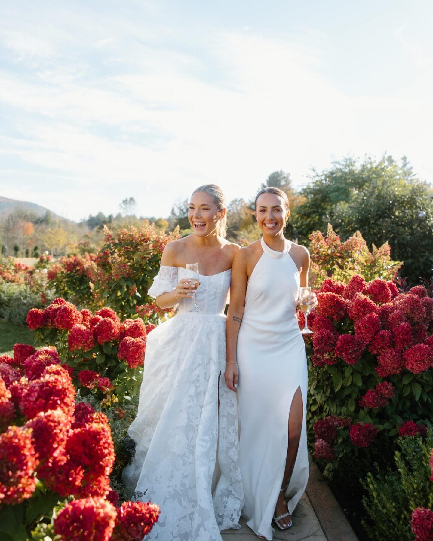 Two women in white dresses standing among red flowers outdoors.