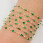 Gold chain bracelet with green beads on a wrist against a white background