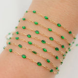 Gold chain bracelet with green beads on a wrist against a white background