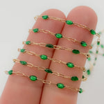 Gold chain with green beads held on a hand against a white background
